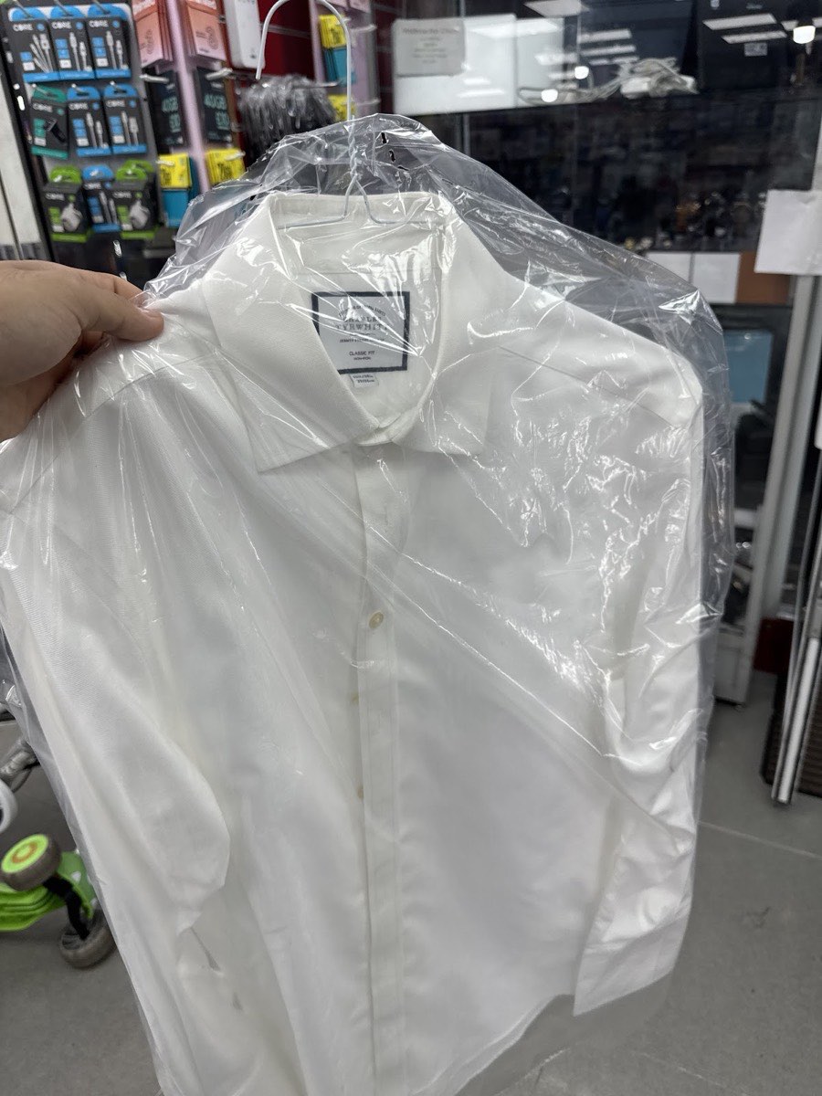 A freshly dry-cleaned white shirt on a hanger, bagged and ready to collect inside Malik Universal Trades