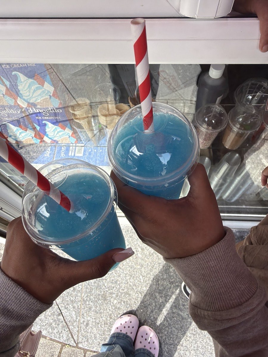 Two bright blue slush drinks with striped paper straws at the ice cream counter in Malik Universal Trades, Barking